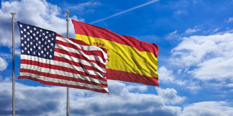 Spain And America Waving Flags On Blue Sky. 3D Illustration
